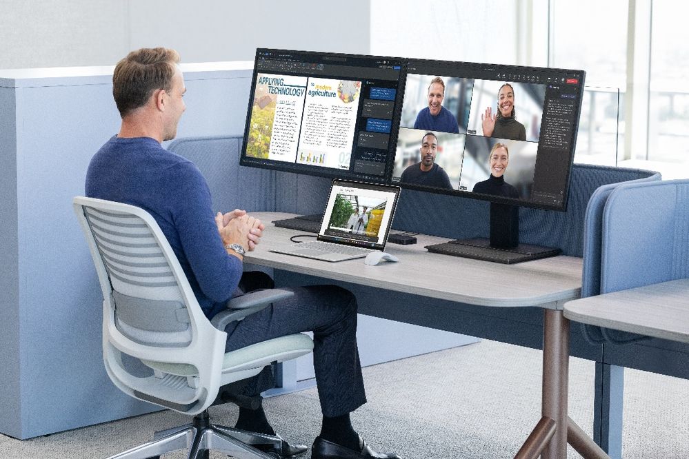 Man sitting at a desk with two monitors and a Surface Laptop on a Teams meeting